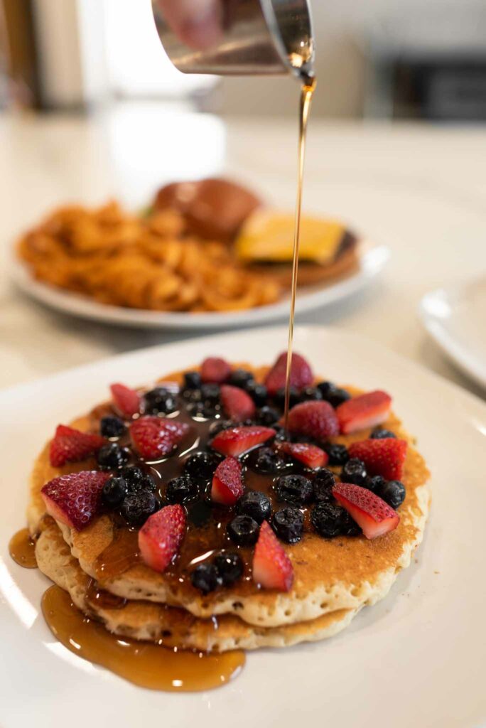 Pancakes with fruit and syrup being poured on top at Jimmy's Egg, an Oklahoma Restaurant.