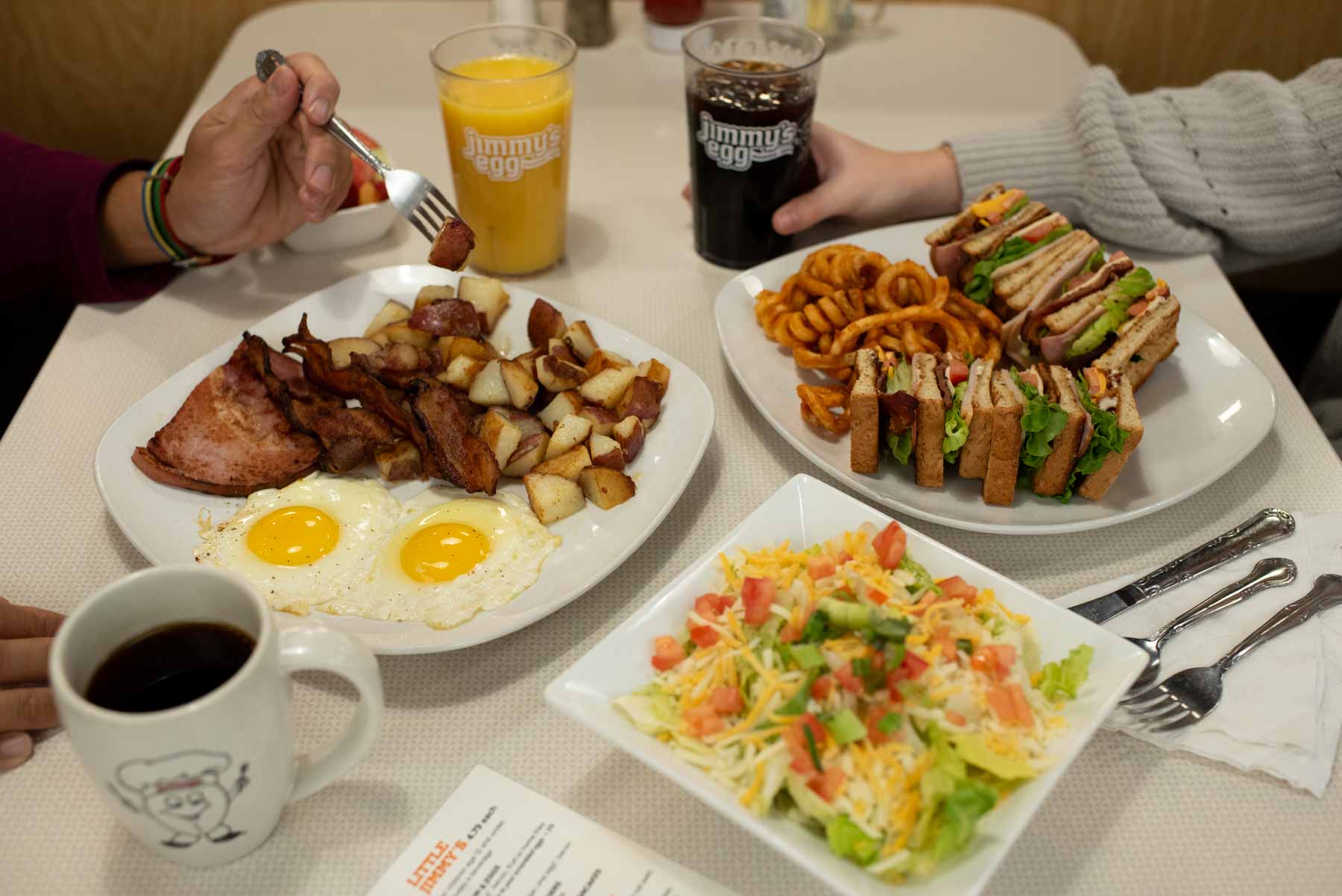 Breakfast and lunch plates and drinks on a table with guests enjoying the meals.