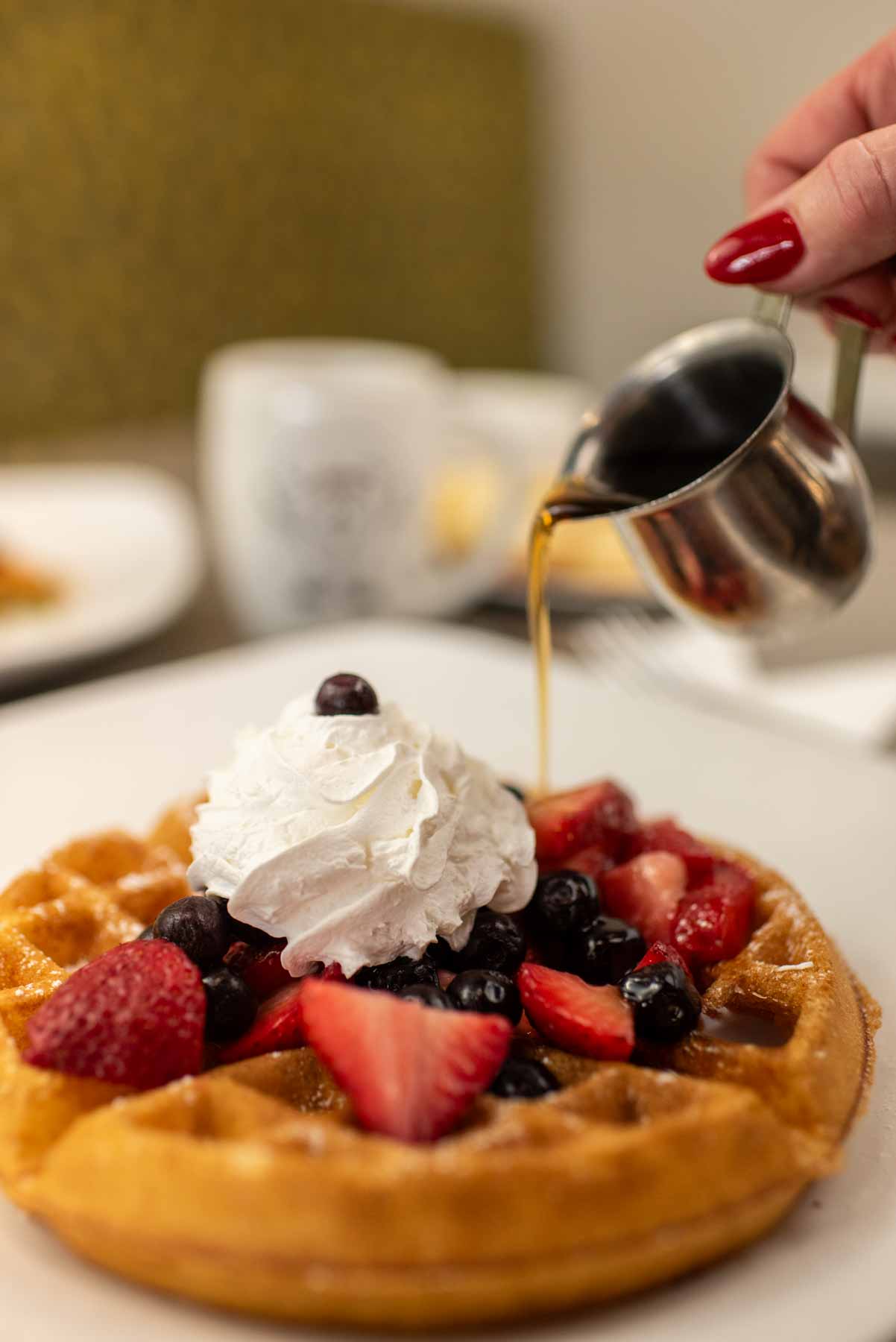 Waffle with fruit and whipped topping with syrup being poured on top at Jimmy's Egg.